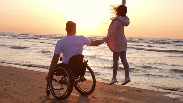 Handicapped man in wheelchair and his girlfriend on a beach at sunset