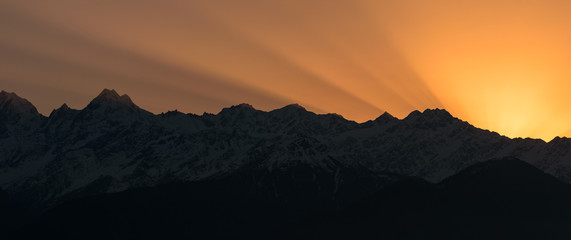 Rays of sunlight in the sky behind the Panchachuli mountains in Munsyari during sunrise.