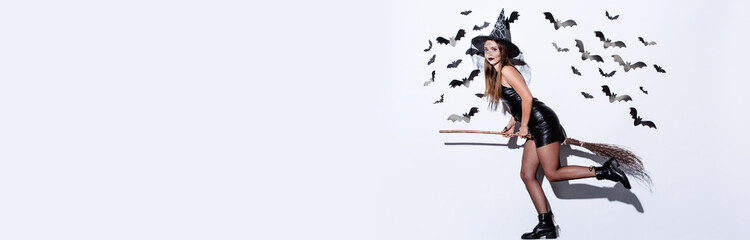 panoramic shot of girl in black witch Halloween costume on broom near white wall with decorative...