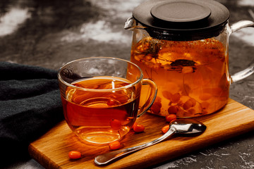 hot spicy tea with sea buckthorn in a glass teapot and Cup, on a dark background.