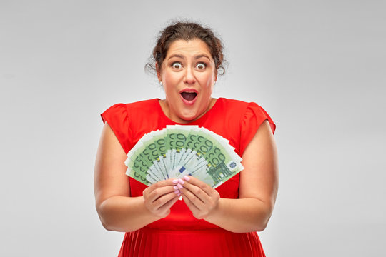 People And Finances Concept - Surprised Woman In Red Dress Holding Hundreds Of Euro Money Banknotes Over Grey Background