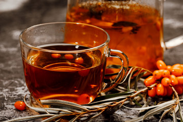 hot spicy tea with sea buckthorn in a glass teapot and Cup, on a dark background.