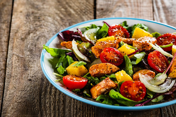 Salad with chicken, mango and tomatoes on wooden table