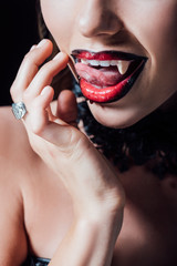 cropped view of scary vampire girl licking fangs isolated on black