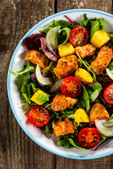 Salad with chicken, mango and tomatoes on wooden table