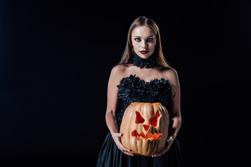 scary vampire girl in black gothic dress holding carved Halloween pumpkin with candles isolated on...