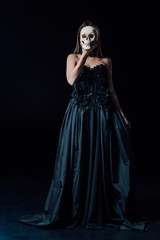 scary vampire girl in black gothic dress holding human skull in front of face