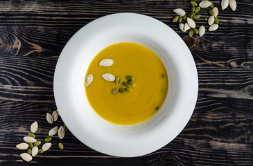 pumpkin soup in white plate natural wood dark background top view