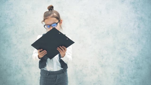 Lady boss schoolgirl standing with folder on gray background. Turning the folder shows the word business. Close-up Slow video.