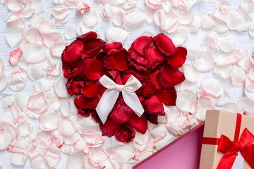 Heart shape created from red rose petals with white ribbon and open empty gift box out standing from light pink rose petals on white wooden background. Top view. Love concept. Gift time.
