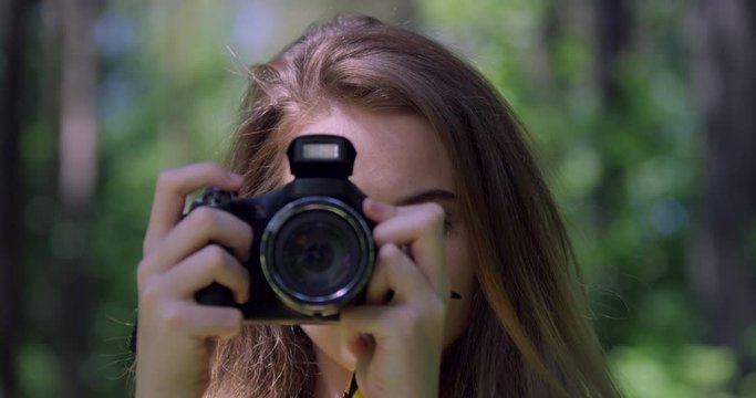 4K Portrait. Girl taken a photograph with Camera in Forest. Young Photography Student in a Wood Glade of Trees. Blonde Hair, Pretty Woman in a British Nature Park with Sun Light.