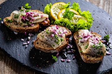 Marinated herring fillets on slices of bread on black stone