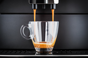 freshly brewed coffee is poured from the coffee machine into glass cup - 293831602