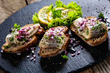 Marinated herring fillets on slices of bread on black stone