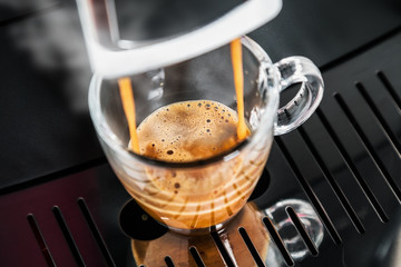 freshly brewed coffee is poured from the coffee machine into glass cups