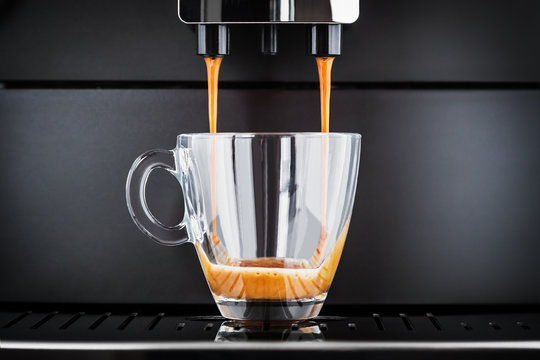 freshly brewed coffee is poured from the coffee machine into glass cup