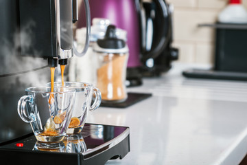 freshly brewed coffee is poured from the coffee machine into glass cups in the kitchen at home