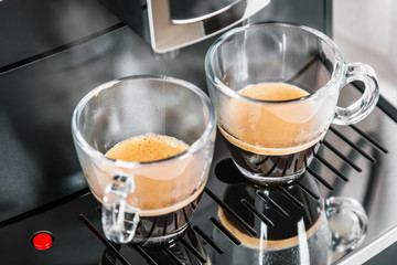 freshly brewed coffee is poured from the coffee machine into glass cups in the kitchen at home
