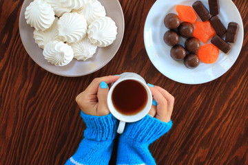 woman's hands, a mug of tea. marshmallows, marmalade, candies on the plates