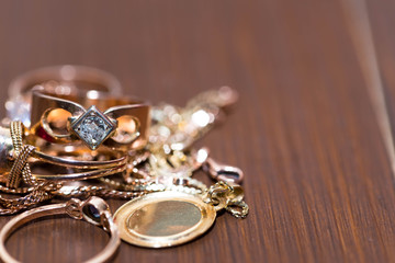 Real gold rings with diamonds, gems, neckless on dark cracked wood background close up macro shot.