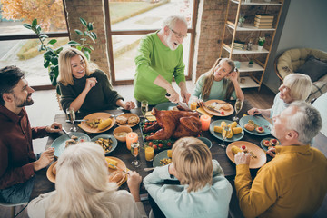 Photo of big family sit feast meals table around blessing roasted turkey eldest grandfather making slices hungry relatives waiting excited in living room indoors