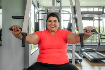Asian Overweight woman playing Gym Equipment to exercising build her boday alone in gym, happy and smile during workout. Fat women take care of health and want to lose weight concept.. - obrazy, fototapety, plakaty