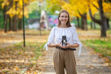 Attractive beautiful young girl holding retro vintage twin lens reflection camera in autumn park.