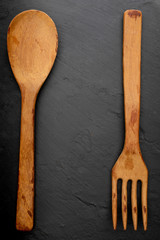 Wooden spoon and fork on textured black chalkboard background. Space to insert your text here. Letter for restaurants. (Food concept of spoon, pot).