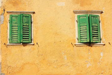 Windows with green shutters on a yellow wall