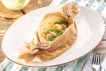 Cooked rice risotto with squid and shrimps in baking paper on white plate on wooden table