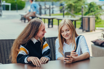 Happy bright positive moments of two stylish girls hugging and looking at the phone, discussing something on the street in the city. 