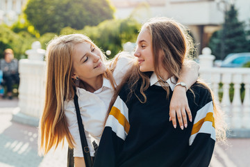 Happy brightful positive moments of two stylish girls hugging on street in city. Closeup portrait funny joyful attarctive young girls having fun, smiling, lovely moments, best friends.