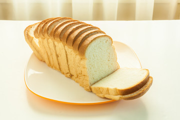 Loaf of bread sliced in a plate on a table near window with sunlight