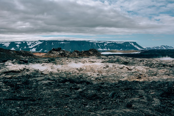 Leirhnjukur old black lava field with colorful stones and smoke coming from ground and blue sky in Iceland, overcast day in summer , film effect with grain