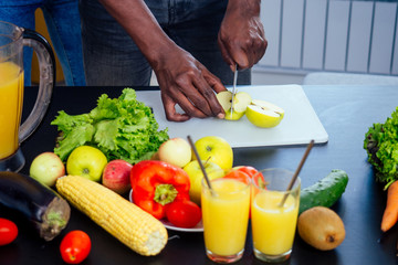 close up photo of afro male hamds cutting apple,eggplant and kivi