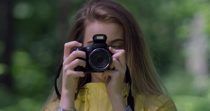 4K Portrait. Young Girl with Camera in a Forest.Young Student taking photographs in Yellow Rain coat and Backpack. Gap Year Traveller with Blonde Hair,Woman in a British National Trust Park