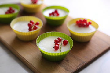 Italian dessert panna cotta with fresh red currants served in silicon molds form on wooden tray and...