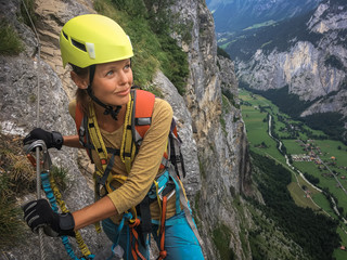 Pretty, female climber on a via ferrata - climbing on a rock in Swiss Alps