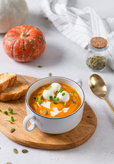 Vegetarian autumn pumpkin cream soup with seeds and mozzarella balls on white background with pumpkins and bread