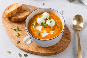 Vegetarian autumn pumpkin cream soup with seeds, mozzarella balls and greenery in white bowl on white background. Menu, restaurant. Vegeterian seasonal food.