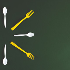 Plastic yellow forks and white spoons on a green background.