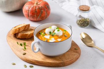 Pumpkin cream soup with coconut milk, pumpkin seeds and mozzarella balls on a white concrete background. Healthy dietary snack and lunch. Place for text. Side view. Menu, restaurant concept