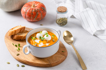 Vegetarian autumn pumpkin cream soup with seeds and mozzarella balls on white background with pumpkins and bread. Copy space. Menu, restaurant. Vegeterian seasonal food.