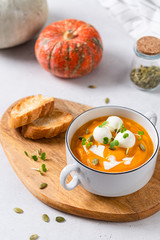 Pumpkin soup in a bowl served with mozzarella balls, greenery and pumpkin seeds on white background with pumpkins and autumn leaves. Vegan soup. Menu, restaurant