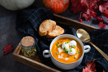 Pumpkin cream soup with coconut milk, pumpkin seeds and mozzarella balls on a dark concrete background. Healthy vegan snack and lunch. Side view. Menu, restaurant concept