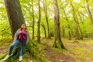 Lady poses leaning on a tree in the forest during a humid morning.