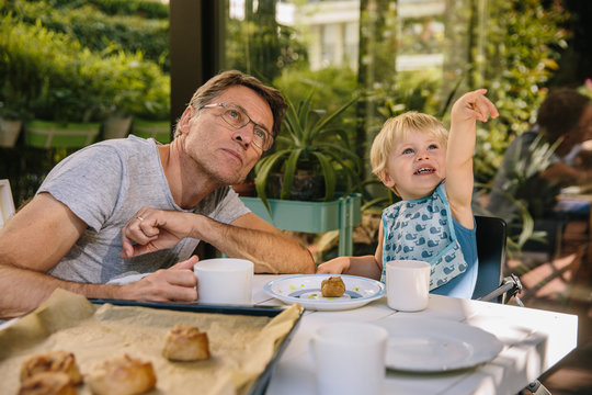 Toddler pointing at something in the sky while having breakfast ourside with his dad
