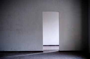 Empty white wall of building without repair, with one door behind which daylight shines, the concept of overcoming difficult situations, finding a solution to the problem