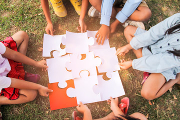 Group of ethnically diverse kids students is joined play jigsaw/puzzles pieces together in the...