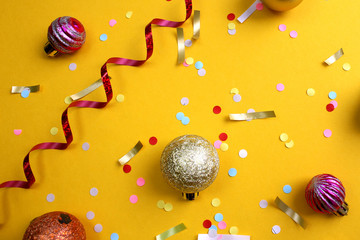 on a yellow background lies a swirling ribbon, festive confetti and balls